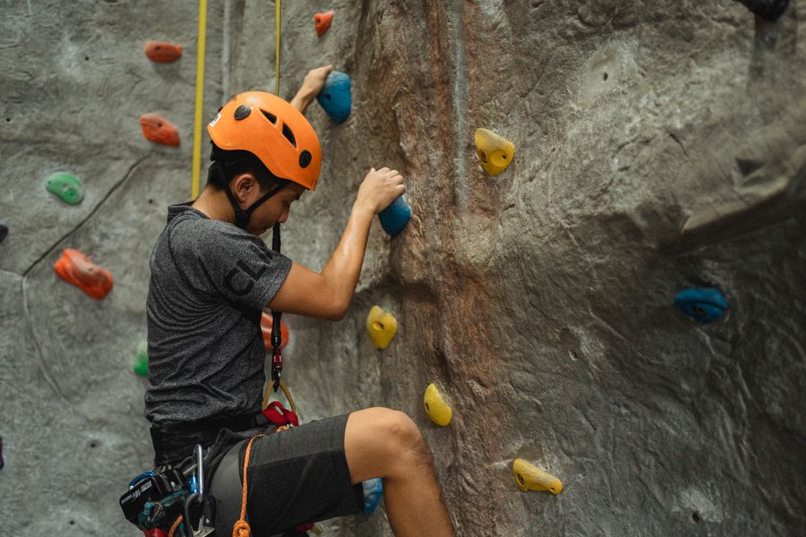 Climber in an orange helmet reaching up for the next hold on a climbing wall