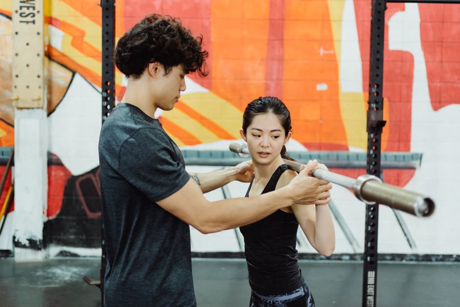 Coach guiding an athlete's hands on the barbell, correcting her lifting technique
