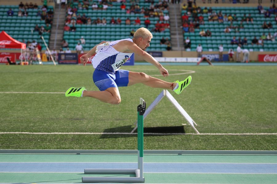 Hurdler mid-flight clearing a barrier in a stadium race