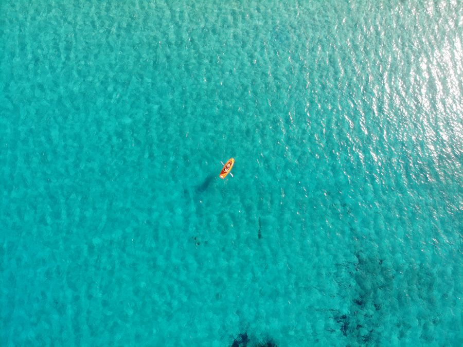 Lone kayaker paddling across a vast open ocean, seen from above